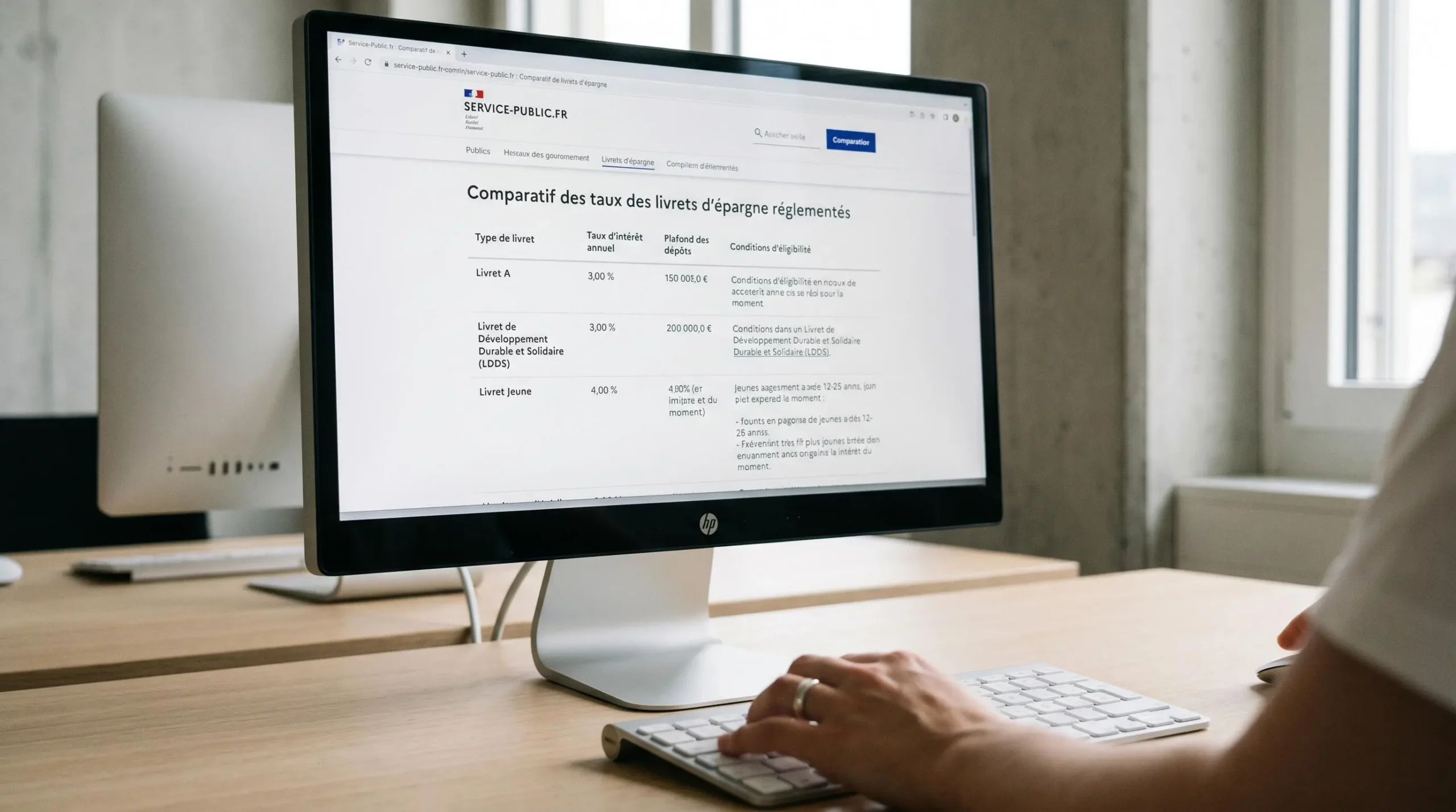 Écran d'ordinateur affichant un tableau comparatif des taux du Livret Jeune et du Livret A sur un site officiel français, main d'utilisateur sur le clavier