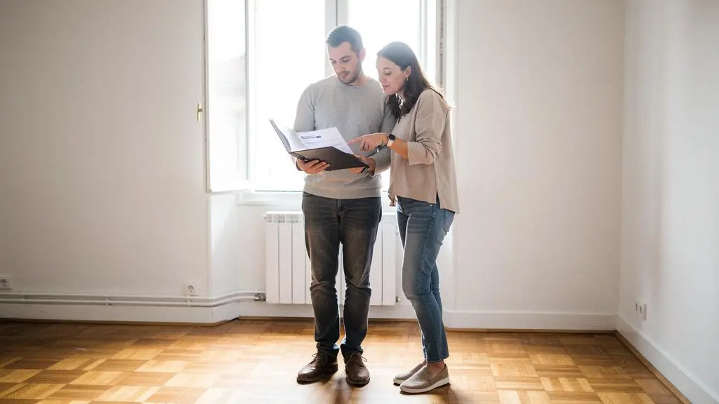 Jeune couple consultant ensemble leurs documents de financement dans un bien immobilier vide lors d'une visite